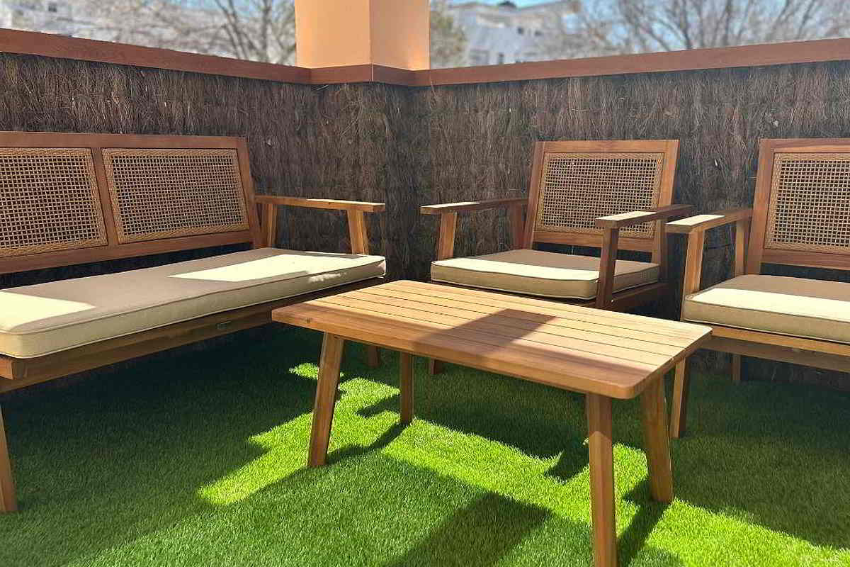 Terraza con mobiliario de madera, cojines beige y césped artificial.
