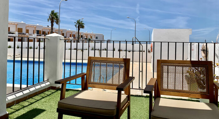 Terraza privada en la Urbanización Las Cañas con vistas a la piscina y mobiliario exterior de madera.