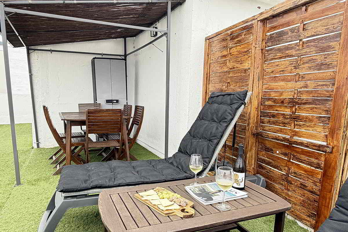 Terraza del apartamento Infinity con tumbona, mesa exterior y zona de comedor cubierta.