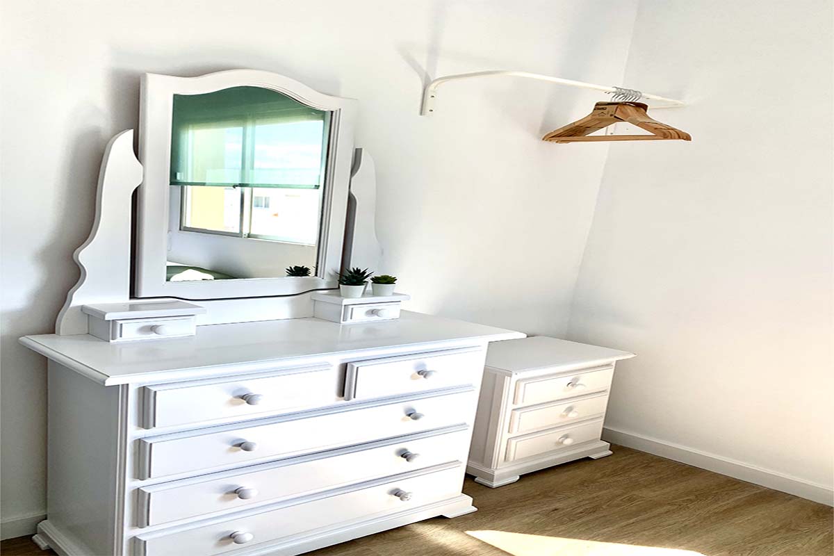 Tocador blanco con espejo y cómoda en una habitación luminosa.