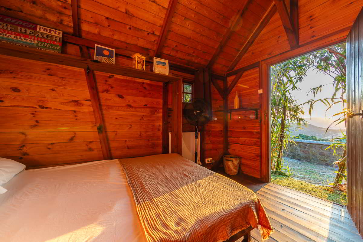 Interior de la cabaña del Chalet La Ahumada con cama doble y puerta abierta que muestra vistas al campo al atardecer.