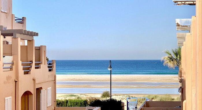 Vista desde el apartamento Los Lances 2 hacia la playa con mar azul y arena dorada entre edificios costeros.