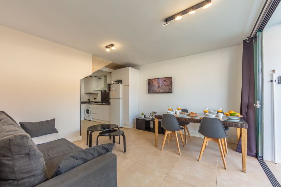 Salón comedor luminoso del apartamento Las Gaviotas 9B en Tarifa con cocina abierta, mesa para cuatro personas y zona de estar integrada.
