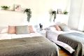 Habitación con dos camas, cojines decorativos y estanterías con plantas verdes.