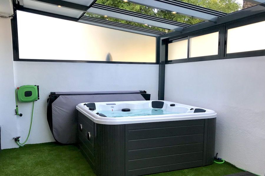 Jacuzzi moderno bajo techo transparente en terraza privada con paredes blancas.