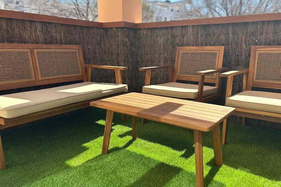Terraza con mobiliario de madera, cojines beige y césped artificial.
