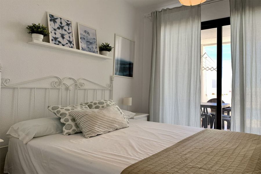 Dormitorio principal con cama doble, decoración delicada y salida a la terraza.