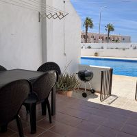 Comedor exterior con mesa negra y sillas, junto a piscina comunitaria con barbacoa.