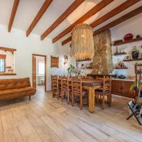 Salón del chalet La Ahumada con techo de vigas de madera, sofá de cuero marrón, gran mesa de comedor rústica y chimenea de piedra, todo decorado con estilo acogedor y natural.
