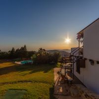 Exterior del chalet La Ahumada con escaleras y jardín al atardecer, vistas abiertas hacia el valle y la piscina rodeada de vegetación.