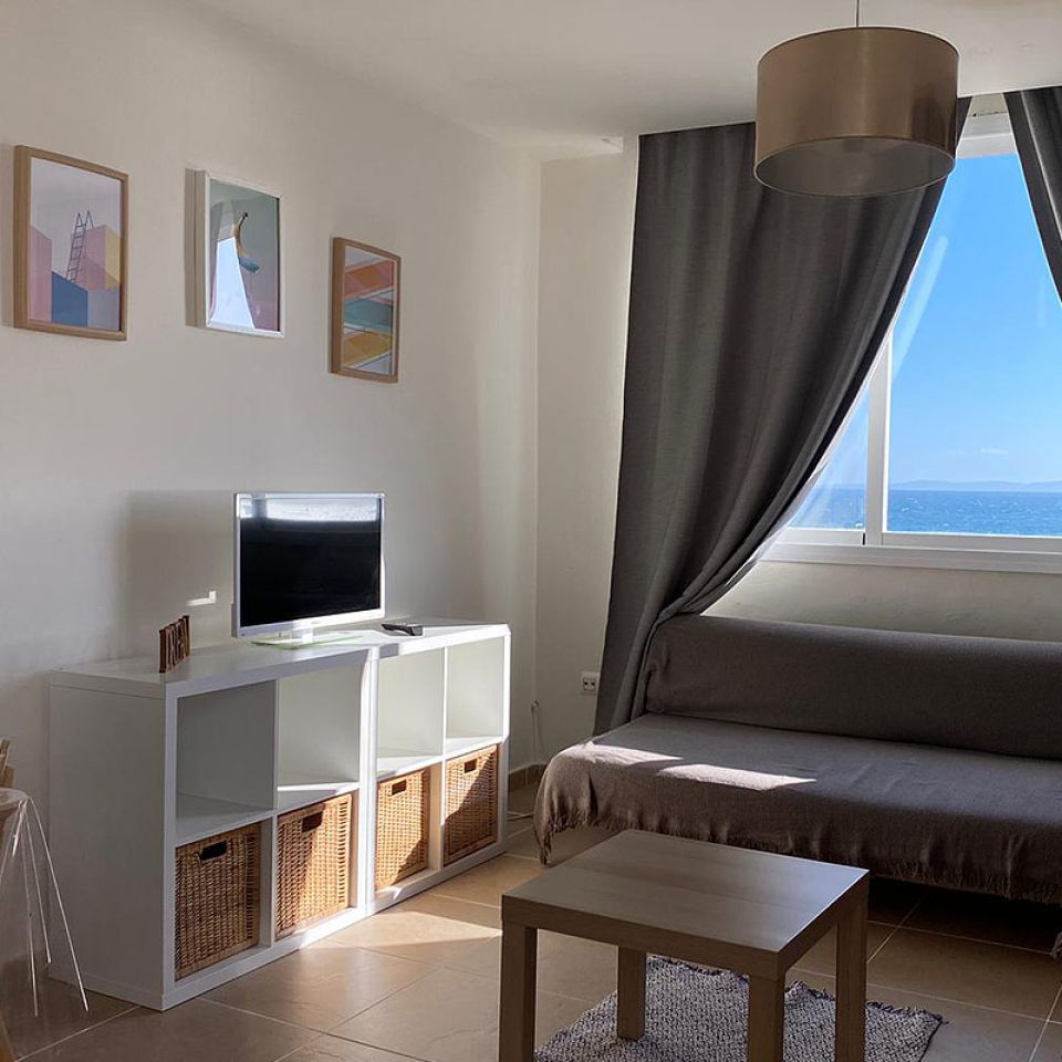 Salón con sofá cama y ventanales con vistas al mar.