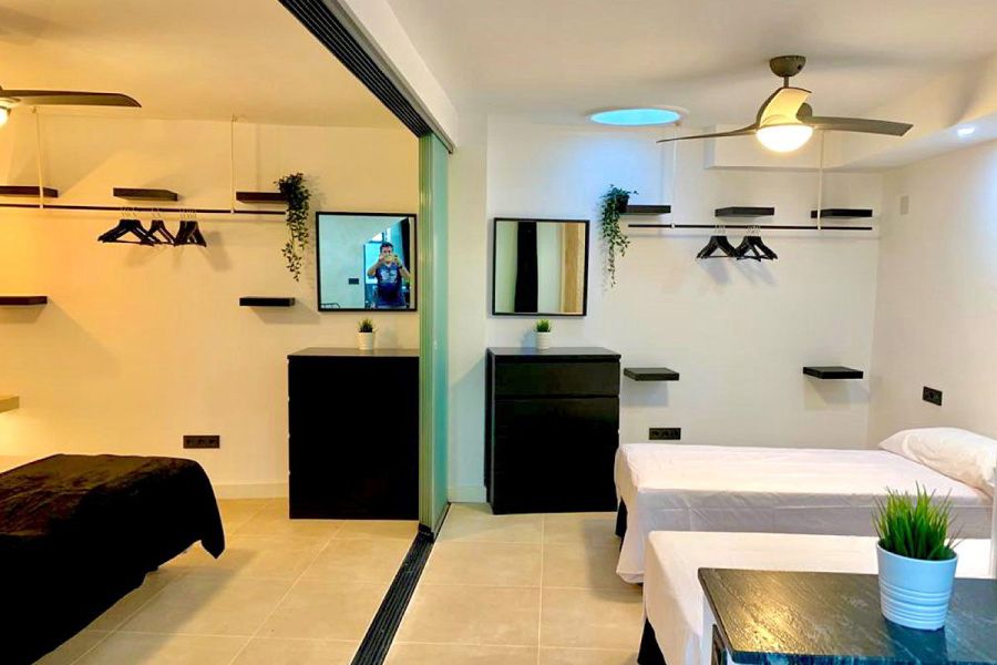 Habitación dividida con cama doble y dos camas individuales, estantes abiertos y ventiladores de techo.