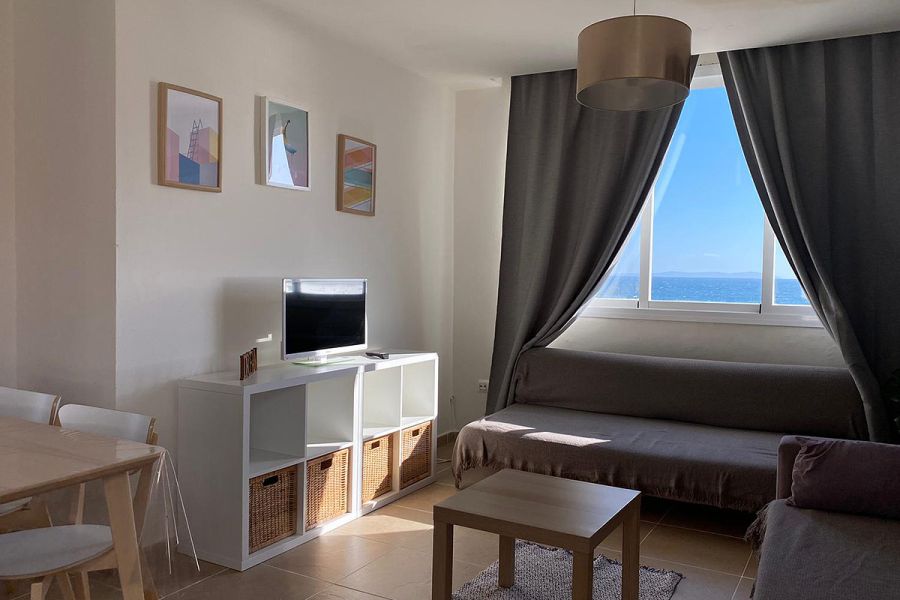 Salón con sofá cama y ventanales con vistas al mar.