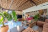 Vista interior del salón y el porche acristalado del Chalet La Ahumada, con sofá en L, televisión, instrumentos musicales y acceso al exterior ajardinado.