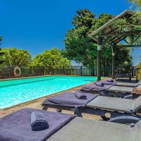 Piscina del Chalet La Ahumada con tumbonas, toallas, pérgola de madera y vegetación alrededor, bajo un cielo azul intenso.
