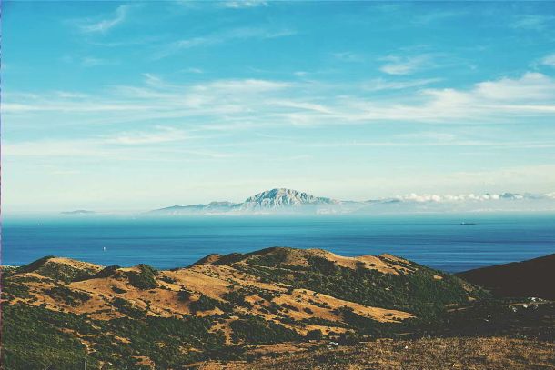 Vista panorámica del Parque Natural del Estrecho con colinas doradas, el mar azul profundo y la costa de África visible al fondo.