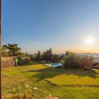 Vista desde una ventana del chalet La Ahumada al gran jardín con piscina y al fondo las montañas al atardecer.