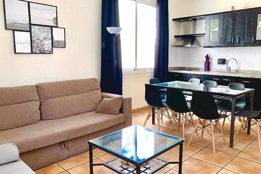 Salón y cocina integrados en el apartamento Wellness, con sofá, mesa de comedor y muebles modernos.