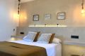 Dormitorio con cama doble, luces colgantes y decoración cálida en tonos beige y blancos.