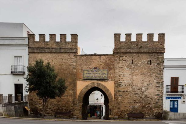 Vista frontal de la Puerta de Jerez, un histórico arco medieval en Tarifa rodeado de casas blancas y detalles de la antigua muralla.