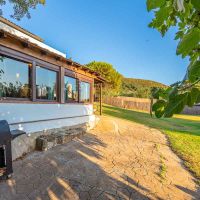 Terraza lateral de Villa Paraíso en Villas La Ahumada, Tarifa, con ventanales de madera, barbacoa, amplio jardín y tumbonas bajo un cielo despejado.