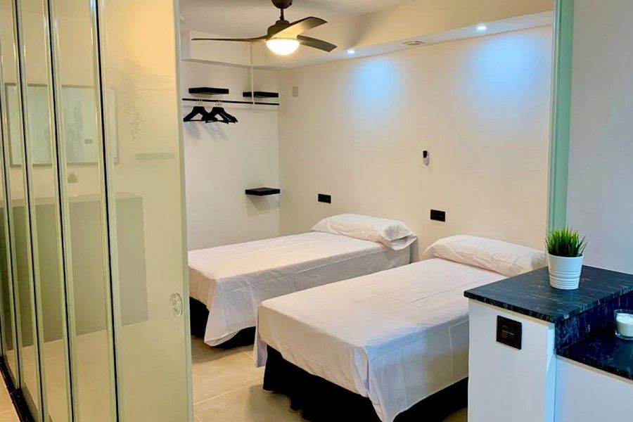 Dormitorio con dos camas individuales, paredes blancas y armario empotrado de vidrio.