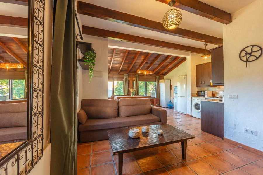Salón de Villa Paraíso en Villas La Ahumada, Tarifa, con sofá marrón, mesa de centro, cocina abierta y comedor acristalado al fondo.