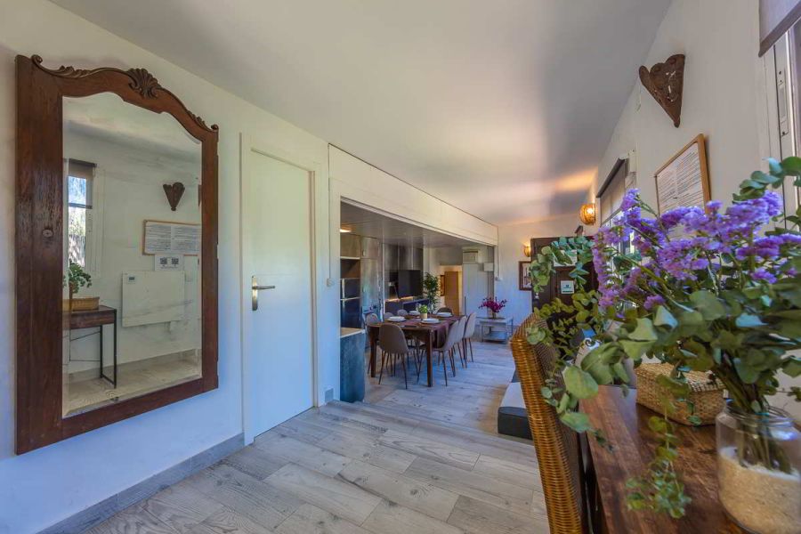 Entrada y pasillo principal de Villa Verde con espejo de madera tallada, flores frescas sobre escritorio rústico, suelo de madera clara y vistas hacia el comedor con luz natura