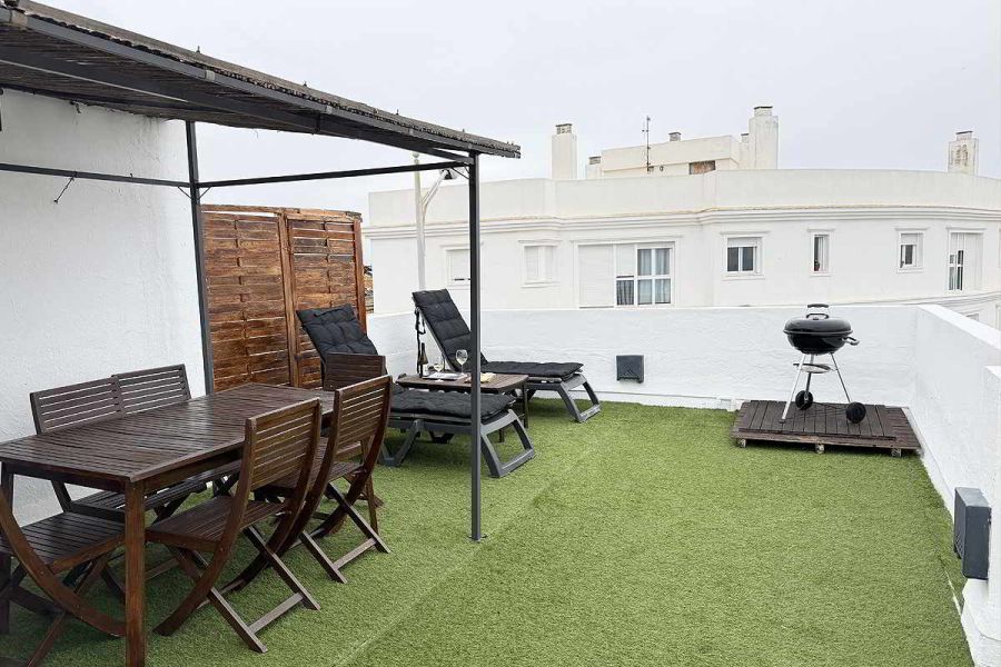 Terraza amplia con comedor exterior, tumbonas y barbacoa en apartamento Infinity.