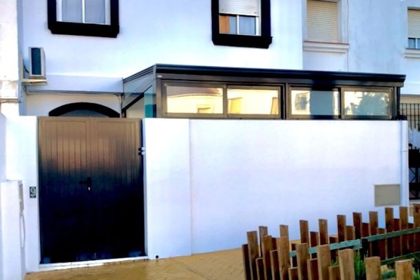 White facade of a semi-detached house with a black door, large windows and stone floor, Las Gaviotas urbanization.