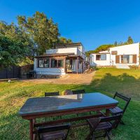 Vista exterior de Villa Paraíso en Villas La Ahumada, Tarifa, con amplia zona ajardinada, mesa de comedor al aire libre y dos edificaciones blancas rodeadas de naturaleza.