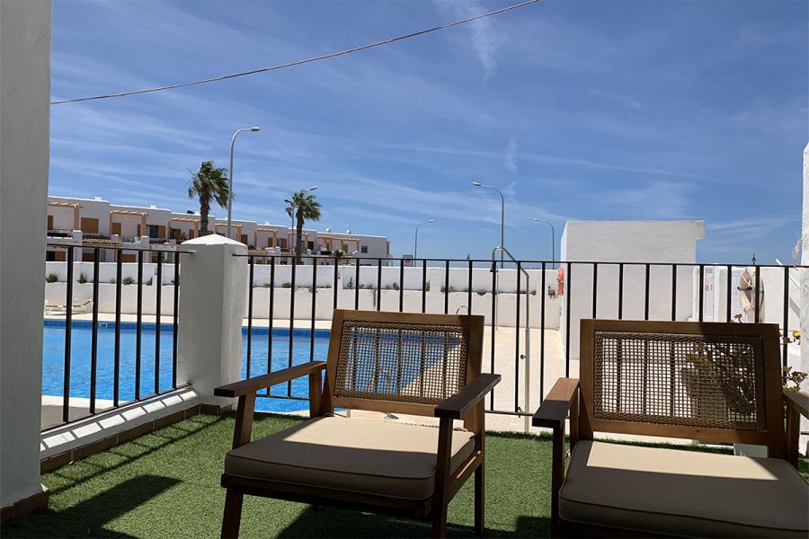 Dos sillas de madera en terraza con vistas a la piscina comunitaria y palmeras al fondo.