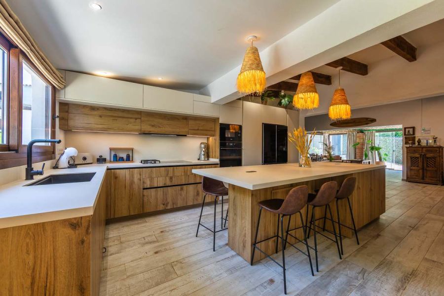Cocina moderna con isla central, taburetes de cuero y lámparas de fibra natural colgantes