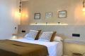 Dormitorio con cama doble, lámparas colgantes, cojines decorativos y detalles de iluminación cálida en pared beige.
