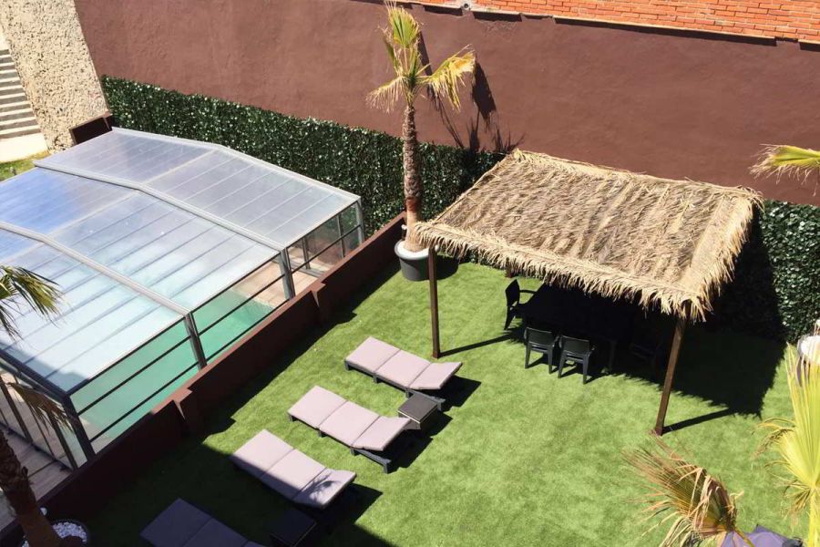 Jardín del Edificio Senses con piscina cubierta, tumbonas y pérgola de madera.