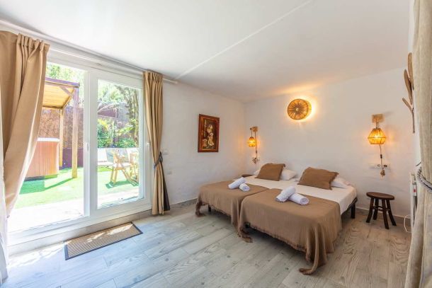 Dormitorio principal de Villa Verde con dos camas individuales juntas, ropa de cama color tierra, lámparas de mimbre encendidas y salida directa al jardín con jacuzzi y tumbonas.