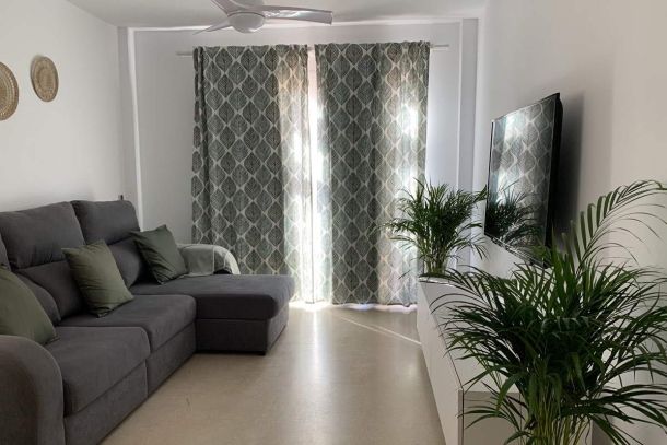 Salón de Los Lances 2 con sofá chaise longue, televisor de pantalla plana y decoración en tonos verdes y neutros.