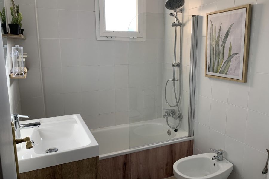 Baño completo en Los Lances 2 con bañera, bidé, lavabo y decoración en tonos blancos y madera.