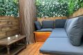 Terraza con sofás de cojines grises, mesa de madera y decoración con plantas verdes
