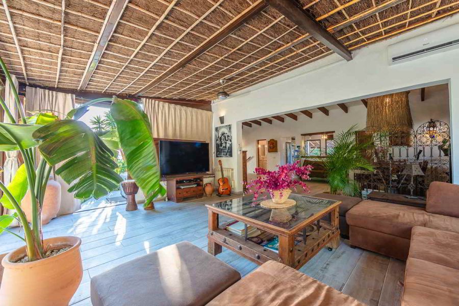Vista interior del salón y el porche acristalado del Chalet La Ahumada, con sofá en L, televisión, instrumentos musicales y acceso al exterior ajardinado.