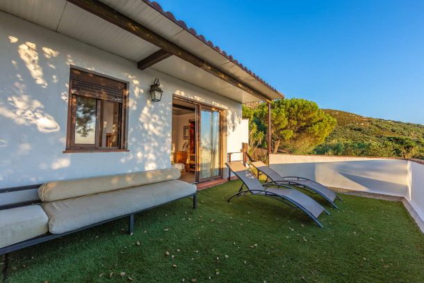Terraza privada de Villa Paraíso, Villas La Ahumada, Tarifa, con césped artificial, sofá acolchado, tumbonas y vistas a las colinas verdes.