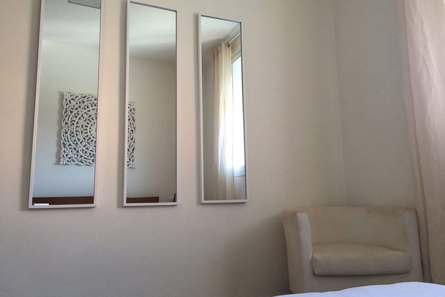 Dormitorio con sillón blanco y tres espejos decorativos en la pared.