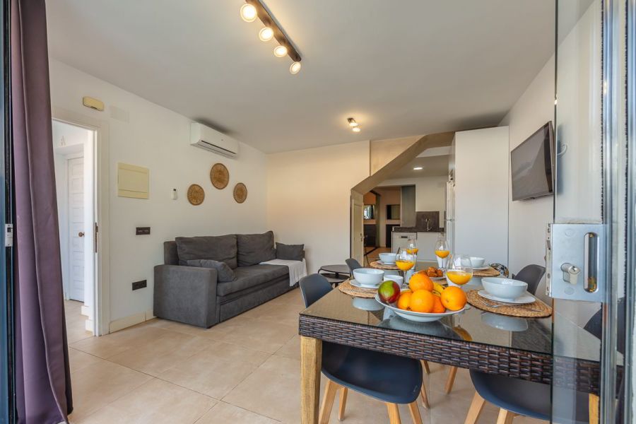 Salón comedor del apartamento Las Gaviotas 9B en Tarifa con mesa para cuatro personas, sofá y cocina abierta al fondo.